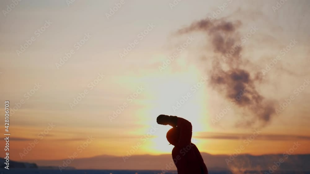 Portrait of person standing on surface of frozen lake at dusk, spilling contents of thermos with beautiful effect of hot water evaporating. Amazing scene demonstration of cool physics effect. Portrait of person standing on surface of frozen lake at dusk, spilling contents of thermos with beautiful effect of hot water evaporating. Amazing scene demonstration of cool physics effect.