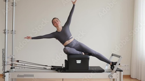 Side view of sportswoman training in the gym on Pilates Reformer machine.