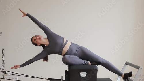 Side view of sportswoman training in the gym on Pilates Reformer machine.