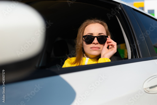 Portrait of redhead young woman lowering sunglasses sitting in white car
