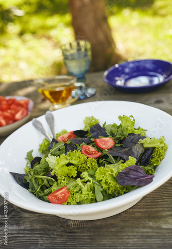 Fresh salad mix of arugula leaves, basil, lambs lettuce and tomatoes. Salad bowl, healthy food. Composition in a white plate on an old wooden table