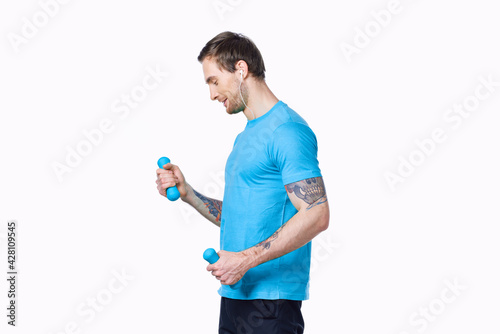 a man doing exercises with dumbbells on a light background in a blue t-shirt and pants © SHOTPRIME STUDIO