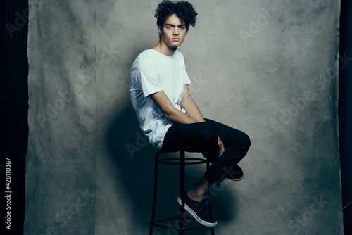 cute guy with curly hair sitting on a chair studio