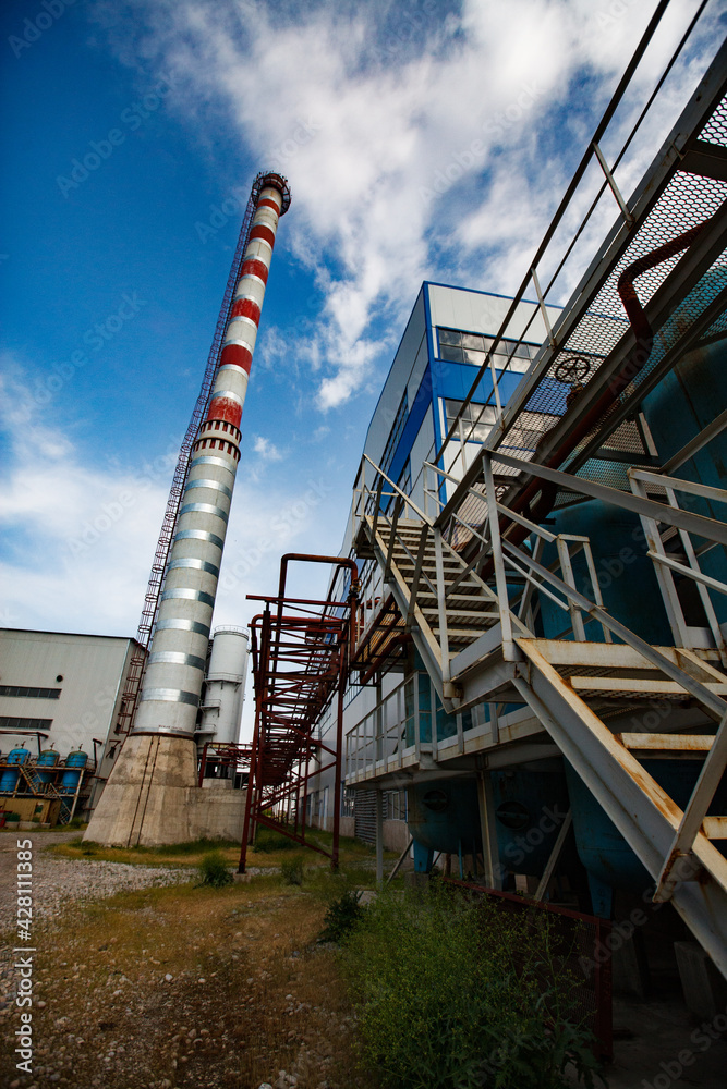 Glass factory Darkhan. Gas power station red and white striped plant chimney and industrial building. Wide-angle view. Blue sky with clouds. Shymkent city, Kazakhstan Glass factory Darkhan. Gas power station red and white striped plant chimney and industrial building. Wide-angle view. Blue sky with clouds. Shymkent city, Kazakhstan