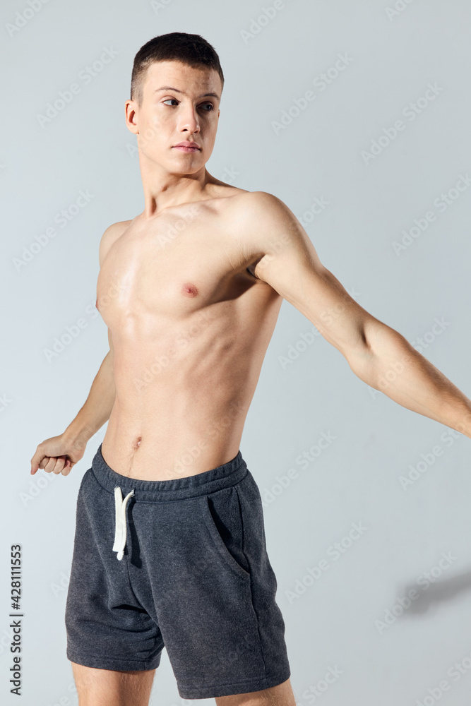 athlete in shorts gestures with his hands on a gray background and bodybuilders workout naked torso