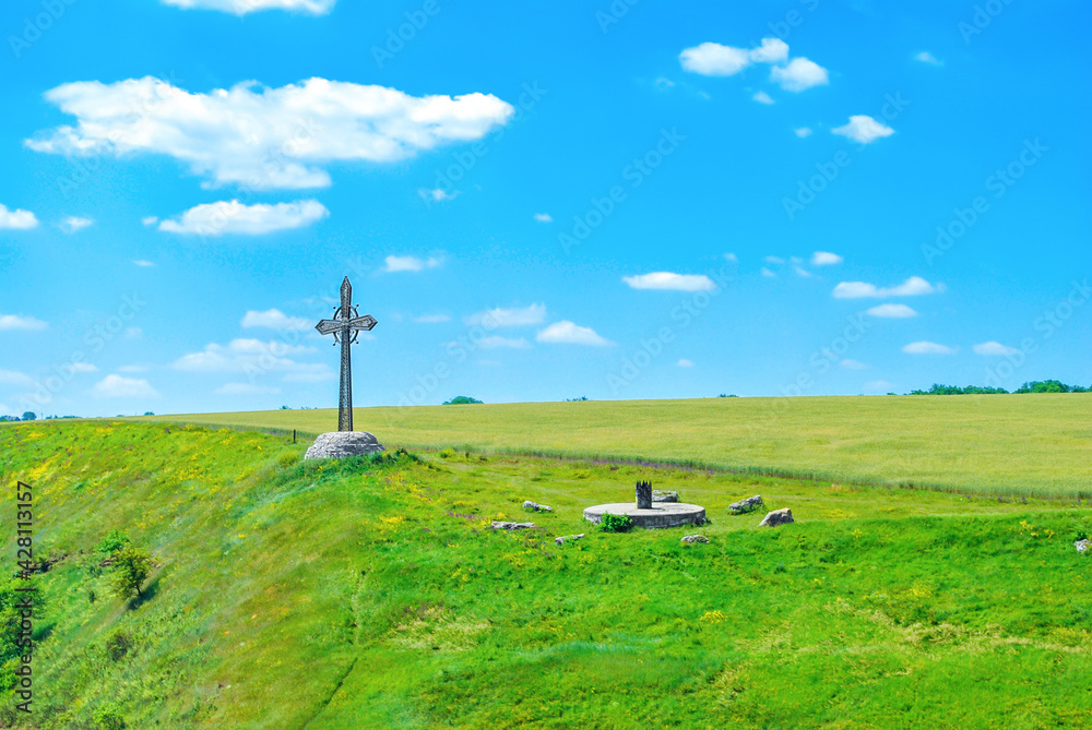 Summer landscape with tall metal cross in green field by blue sky, selective focus Summer landscape with tall metal cross in green field by blue sky, selective focus