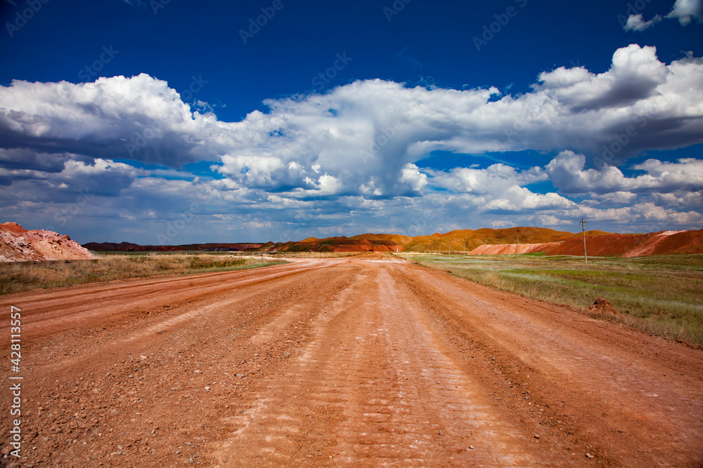Colorful landscape of bauxite mine (aluminium ore quarry). Orange soil and road and blue sky with clouds.