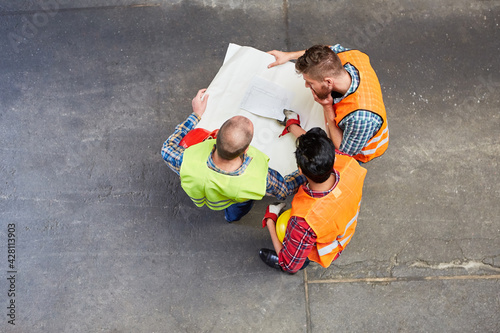 Gruppe Arbeiter mit Bauplan von oben auf Baustelle photo