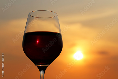 Glass with red wine on sunset background, evening sun is shining through the glass. Concept of celebration, wine industry