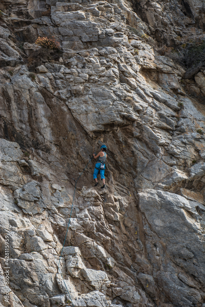 A climber climbing a rock wearing a helmet, using gear A climber climbing a rock wearing a helmet, using gear