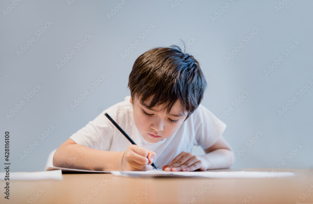 Kid holding pencil writing on white paper, Child boy is drawing, Portrait of school kid doing homework alone, Elementary homeschooling, New normal life style children learning at home Kid holding pencil writing on white paper, Child boy is drawing, Portrait of school kid doing homework alone, Elementary homeschooling, New normal life style children learning at home