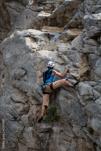 A climber climbing a rock wearing a helmet, using gear