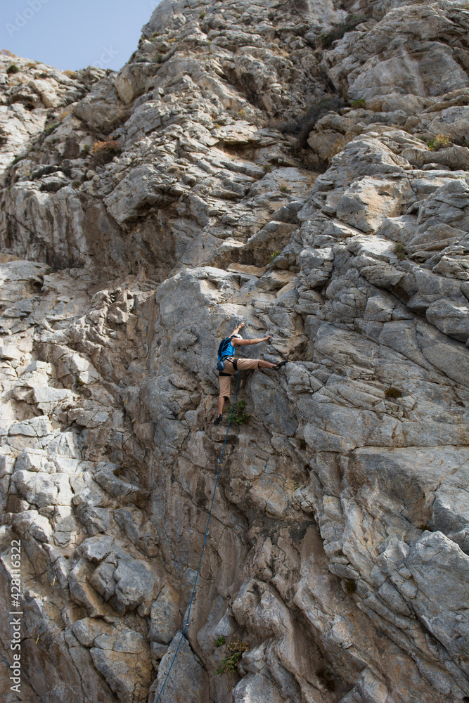 A climber climbing a rock wearing a helmet, using gear