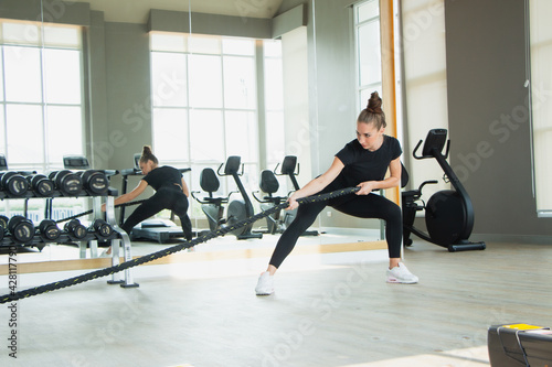 Beautiful woman caucasian white exercising in fitness gym has background exercise equipment.Athletic female exercising with battle ropes at gym