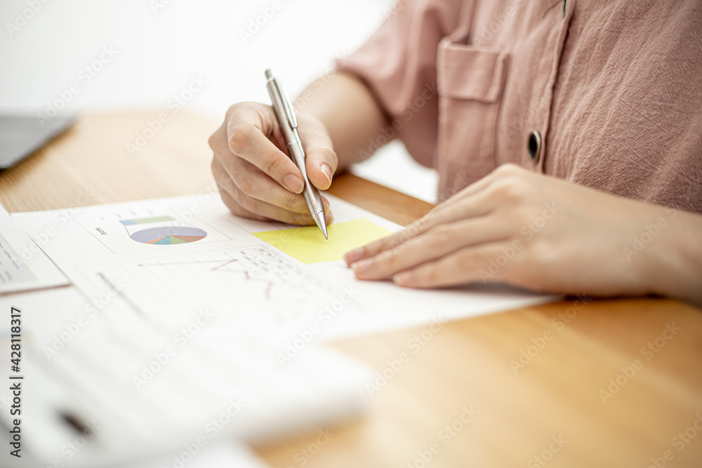 A businesswoman is taking notes on a note on a company financial information sheet for a meeting with a partner, taking important notes on a note on the main meeting papers. Financial concept. A businesswoman is taking notes on a note on a company financial information sheet for a meeting with a partner, taking important notes on a note on the main meeting papers. Financial concept.