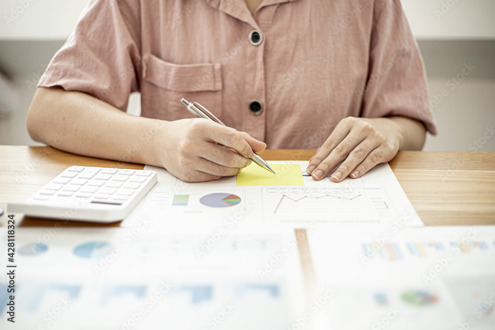 A businesswoman is taking notes on a note on a company financial information sheet for a meeting with a partner, taking important notes on a note on the main meeting papers. Financial concept.