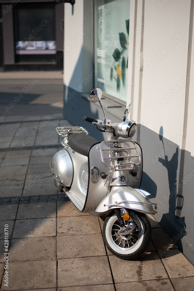 Silver scooter parked outside on a sunny day. Moped