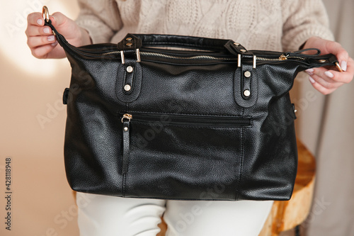a black leather bag in the girl's hands on a beige background.