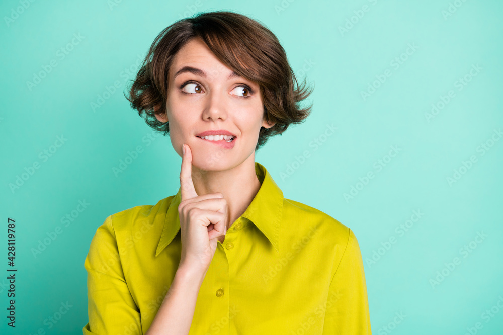 Photo portrait of curious thoughtful girl biting lip looking empty space isolated on bright teal color background Photo portrait of curious thoughtful girl biting lip looking empty space isolated on bright teal color background
