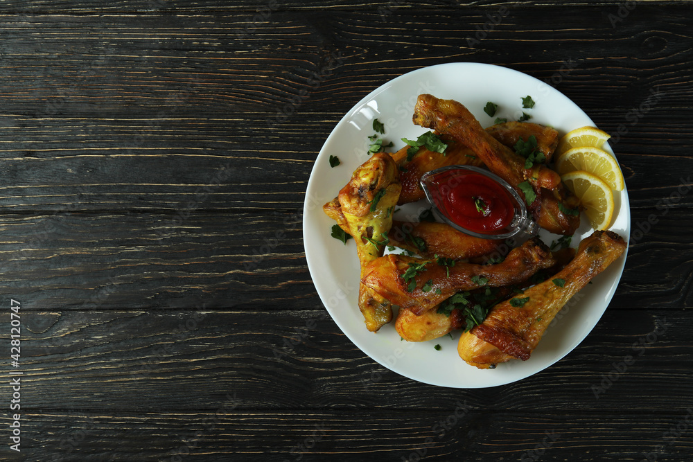 Concept of delicious eating with plate of roast chicken drumsticks on wooden background