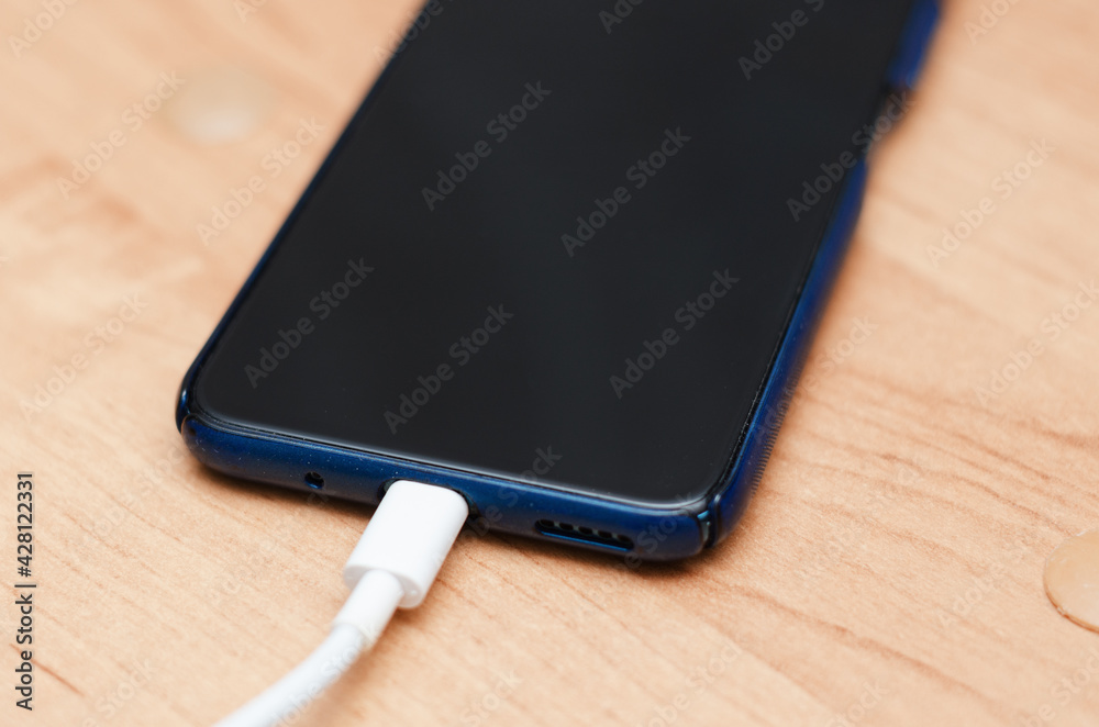the mobile phone is lying on the table with the charging cable connected the mobile phone is lying on the table with the charging cable connected
