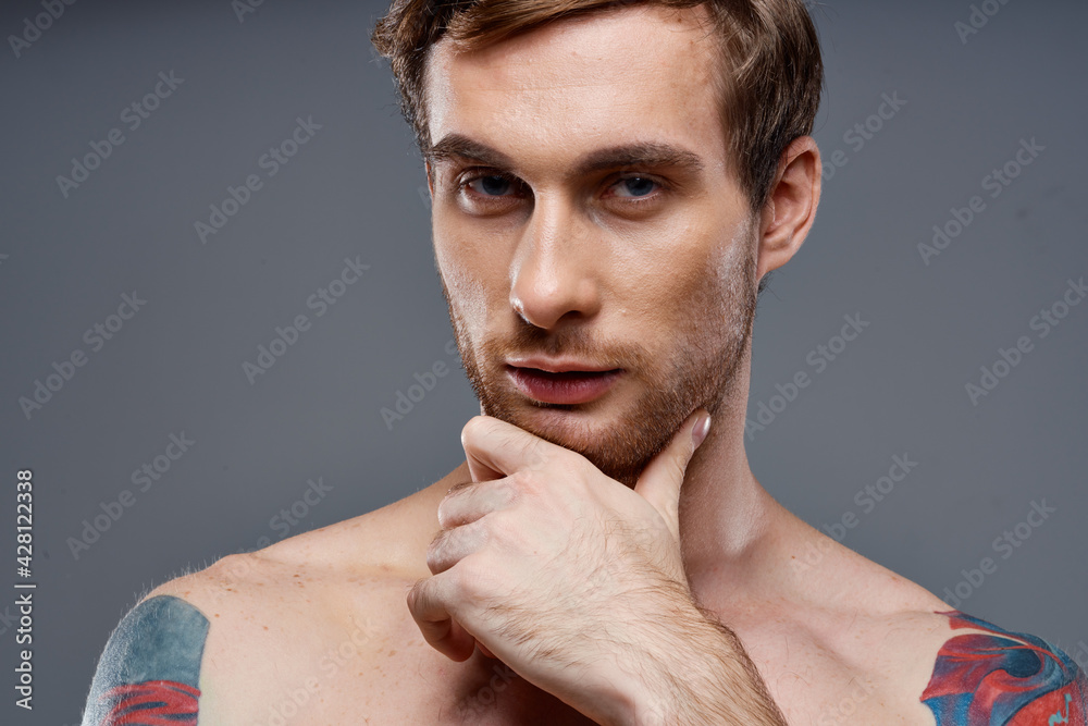 portrait of young man with tattoos on gray background and beautiful face model cropped view portrait of young man with tattoos on gray background and beautiful face model cropped view
