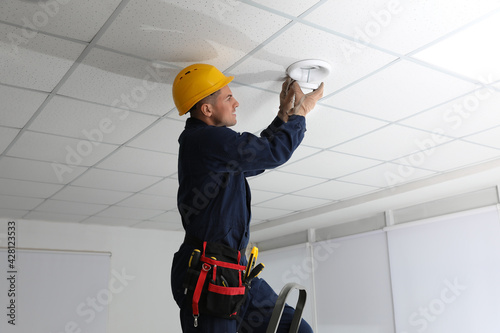 Electrician in uniform repairing ceiling lamp indoors