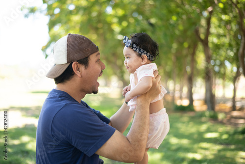 Happy Asian father holding a cute little baby girl on blured background of green garden,  father looking at baby