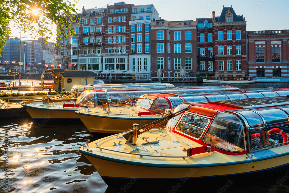 Tourist boats moored in Amsterdam canal pier on sunset