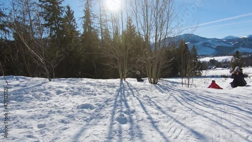 Sledding down the hill from point of view in slow motion during winter sunny day in Zakopane. Chasing kid in red jacket on sleds.