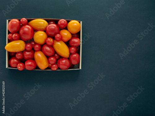 Red and yellow tomatoes in a cardboard box on a dark background with copy space