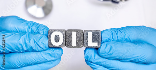 OIL - word from stone blocks with letters holding by a doctor's hands in medical protective gloves