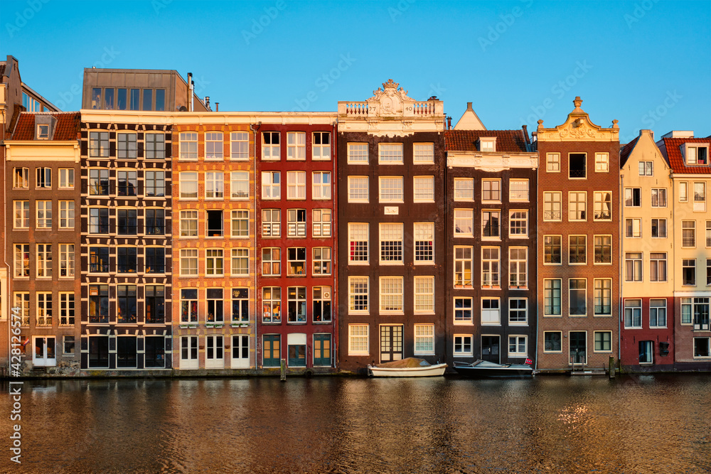 Hhouses and tourist boats on Amsterdam canal pier Damrak on sunset