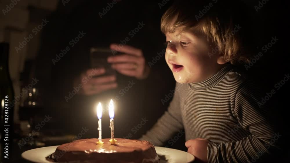 Cute child blowing birthday candles. Toddler boy celebrates anniversary, relighting magic candle