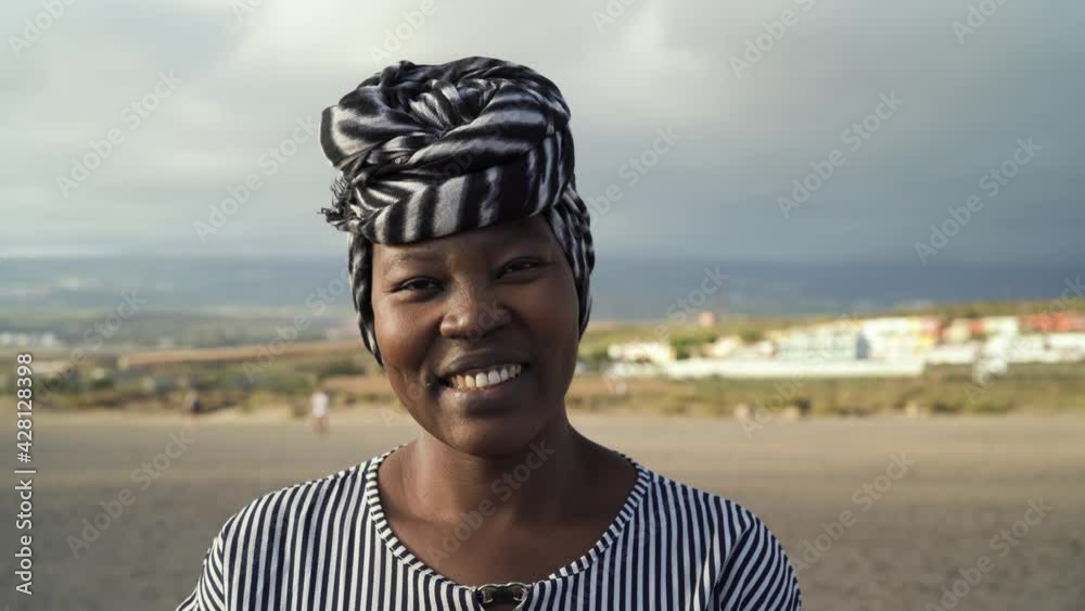 Happy Muslim African woman wearing turban smiling in camera on the beach during summer vacation