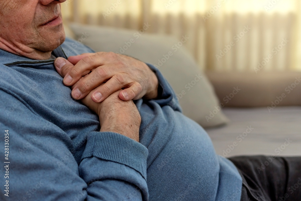 Worried senior man feeling unwell and having chest pain in the living room. Elderly man suffering from heart attack at home. Mature man feeling chest pain while sitting in the living room at home. Worried senior man feeling unwell and having chest pain in the living room. Elderly man suffering from heart attack at home. Mature man feeling chest pain while sitting in the living room at home.