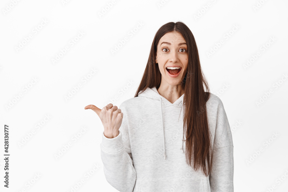 Excited and surprised girl looking happy, pointing aside at left copy space, showing interesting promotional text, recommend follow link, click on banner, standing over white background Excited and surprised girl looking happy, pointing aside at left copy space, showing interesting promotional text, recommend follow link, click on banner, standing over white background