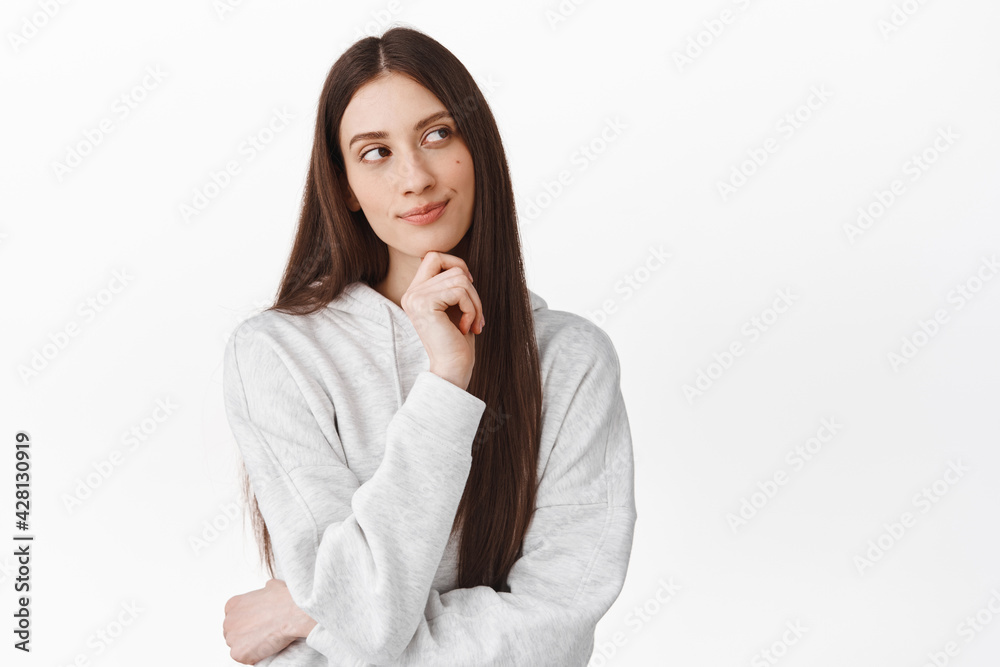 Hmm interesting. Thoughtful cute girl with long hair looking aside and smiling while thinking, standing pensive, making choice, imagine something interesting, white background Hmm interesting. Thoughtful cute girl with long hair looking aside and smiling while thinking, standing pensive, making choice, imagine something interesting, white background