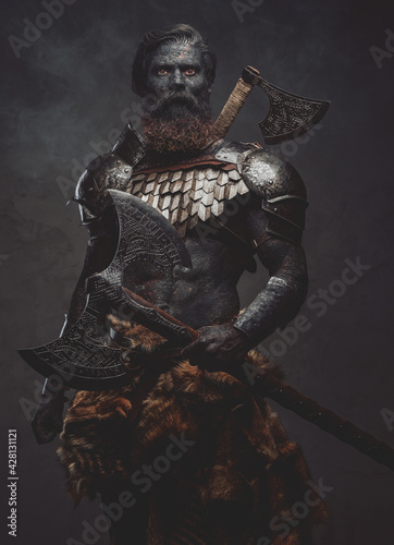 Proud and evil barbarian with two axes posing in dark background