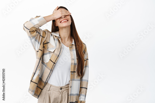 Cuadro en lienzo Happy candid woman covers her eyes with hand and smiles, waiting for surprise, a