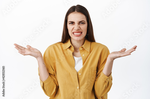 Clueless girl spread hands sideways and cringe, grimacing from something awful or disgusting, cant understand what do, know nothing, standing confused against white background photo