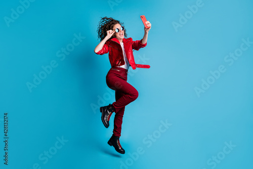 Fototapeta Naklejka Na Ścianę i Meble -  Full length profile photo of attractive cool girl jump make selfie touch round sunglass isolated on blue color background