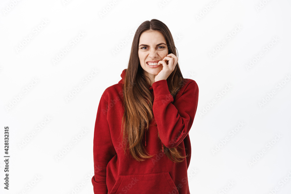 Nervous young woman with bad habits, biting fingernails and looking worried, anxious or concerned about something, looking at camera, standing against white background Nervous young woman with bad habits, biting fingernails and looking worried, anxious or concerned about something, looking at camera, standing against white background