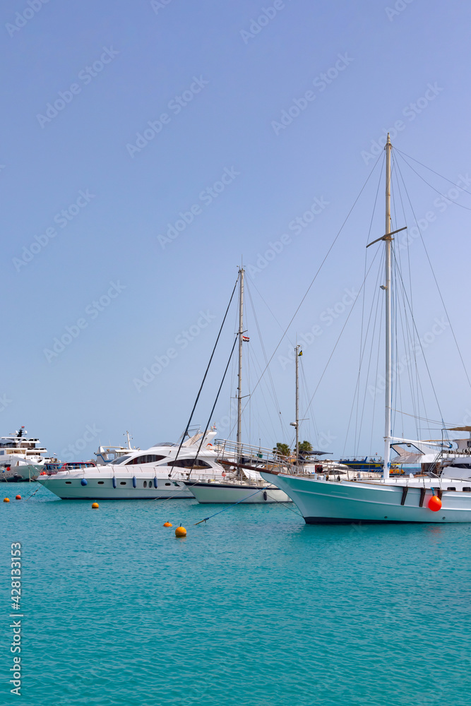 White motor and sailing yachts moored in the azure waters of the Red Sea in the harbor of Hurghada. Clear blue skies echo the color of the sea