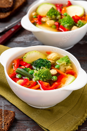 Vegetable soup with broccoli, romanesco, pepper, zucchini, and peas in a white bowl. Vegan soup, diet food.