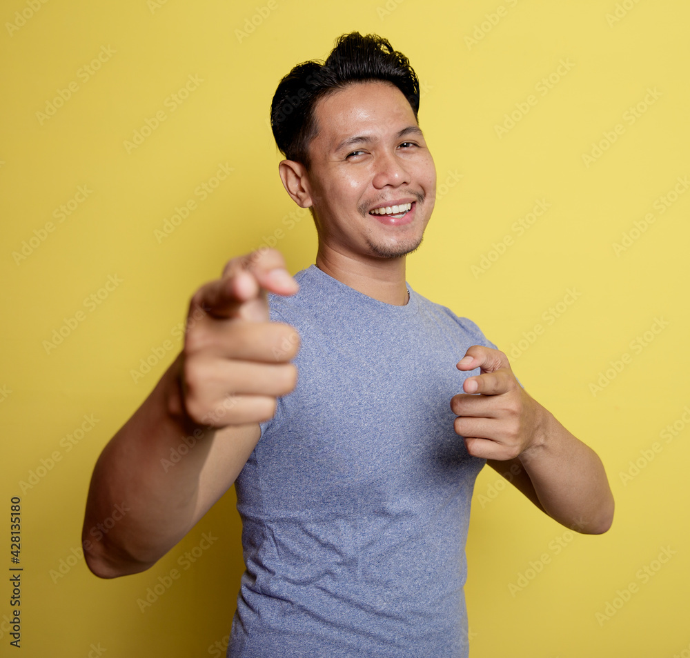 casual young man pointing the camera very happy isolated on a yellow color background casual young man pointing the camera very happy isolated on a yellow color background