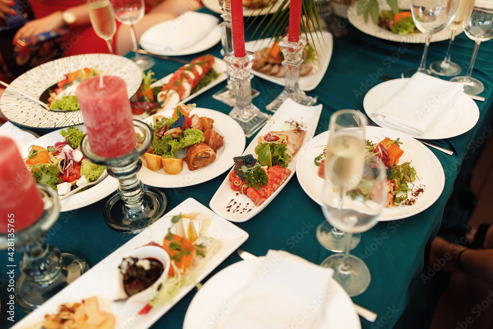 A table on the terrace with many dishes decorated with pink candles. Gala dinner at the bachelorette party. Plates with food on a green tablecloth