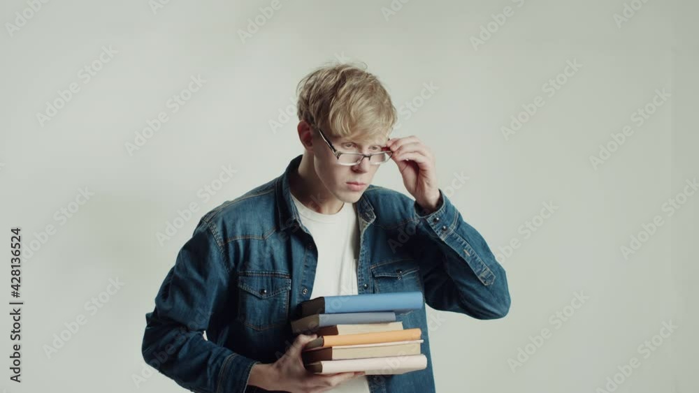 Student man putting on glasses, holding books, thinking. Smart guy looking in camera with thoughtful face, Young male model student standing and posing in studio. Student man putting on glasses, holding books, thinking. Smart guy looking in camera with thoughtful face, Young male model student standing and posing in studio.