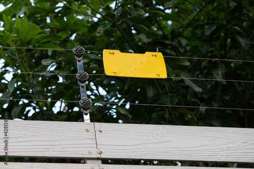 high voltage security fence on house wall with blank yellow plastice sign. photo