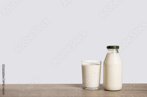 Bottle and glass of milk on wooden table with grey background.